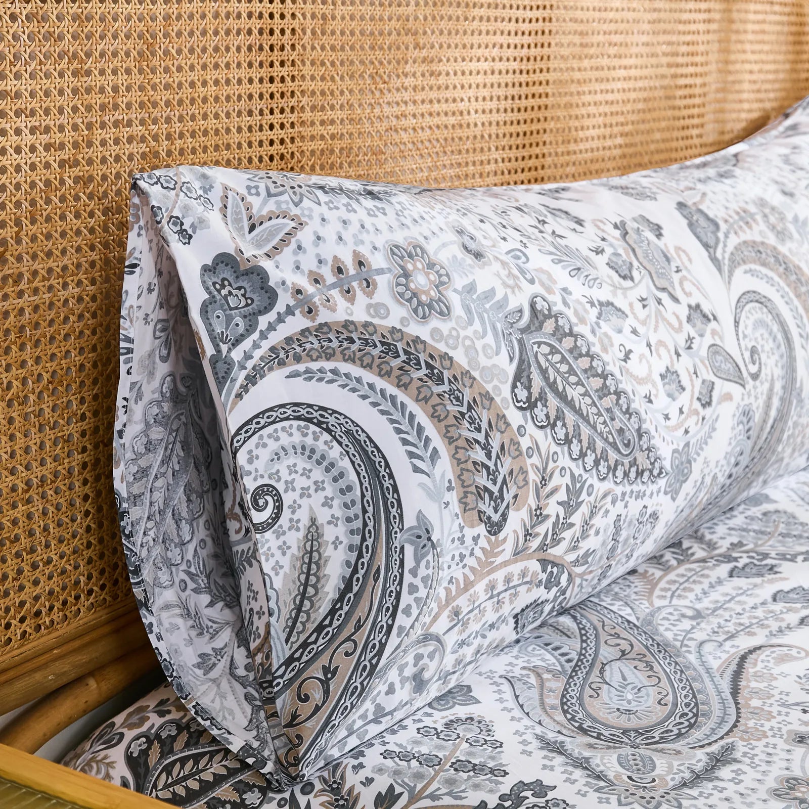 A close-up, angled view of the end of a grey paisley cotton pillowcase, highlighting the envelope closure and the intricate fabric design