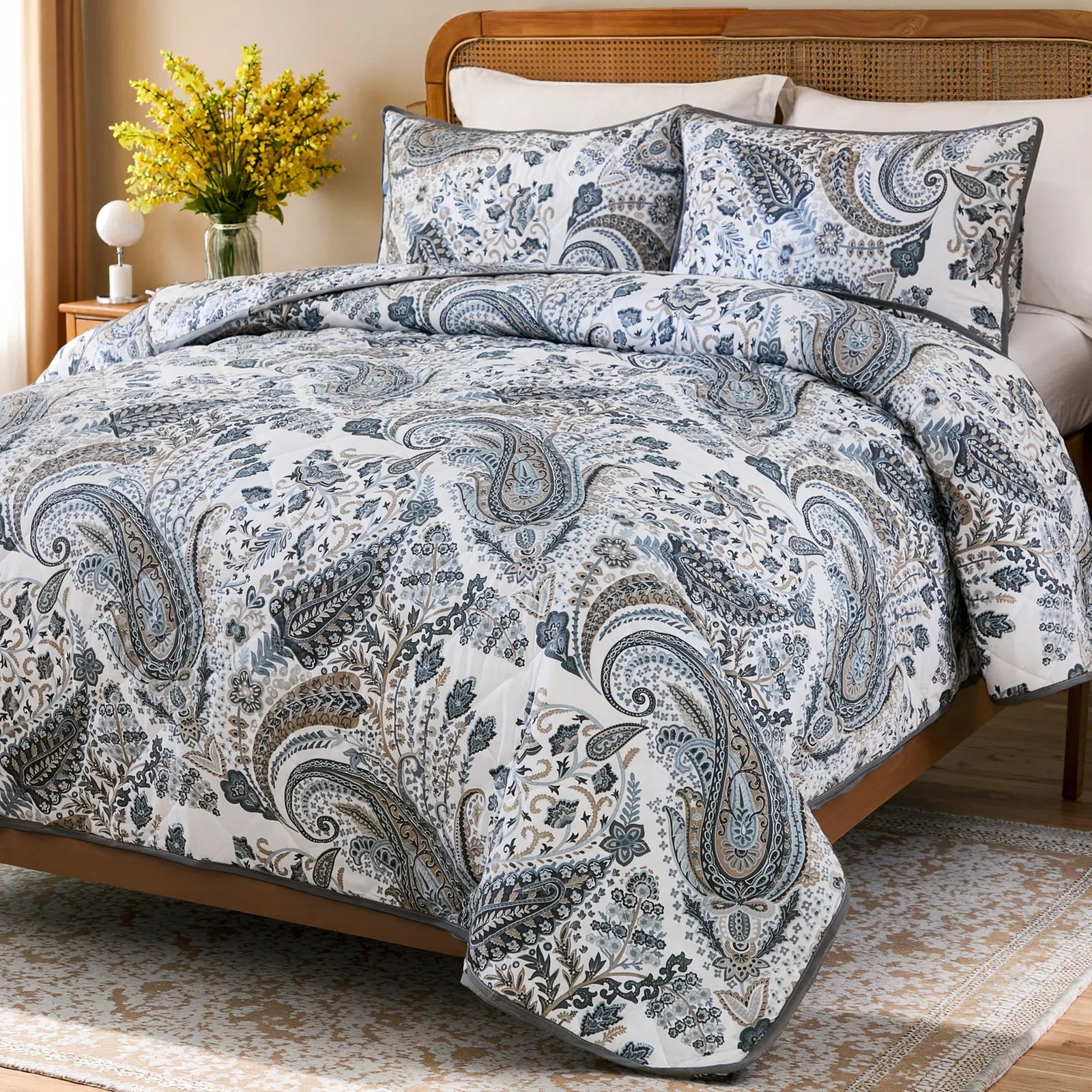 An inviting angled view of the grey paisley quilt set with matching shams.