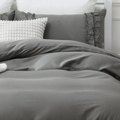 the grey ruffled comforter set styled on a bed in a bright bedroom.