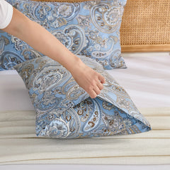 A hand gently pulls open the end of a light blue paisley print cotton pillowcase, revealing its quality and envelope closure.