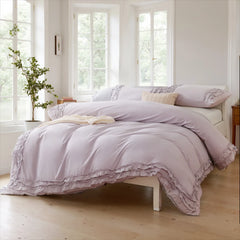 Lavender cotton double ruffle duvet cover on a white wood bed in a bright room with three large windows.