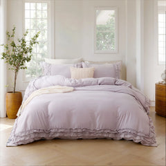 Foot-of-bed view of a lavender cotton ruffle bedding set with a throw blanket and a potted plant.