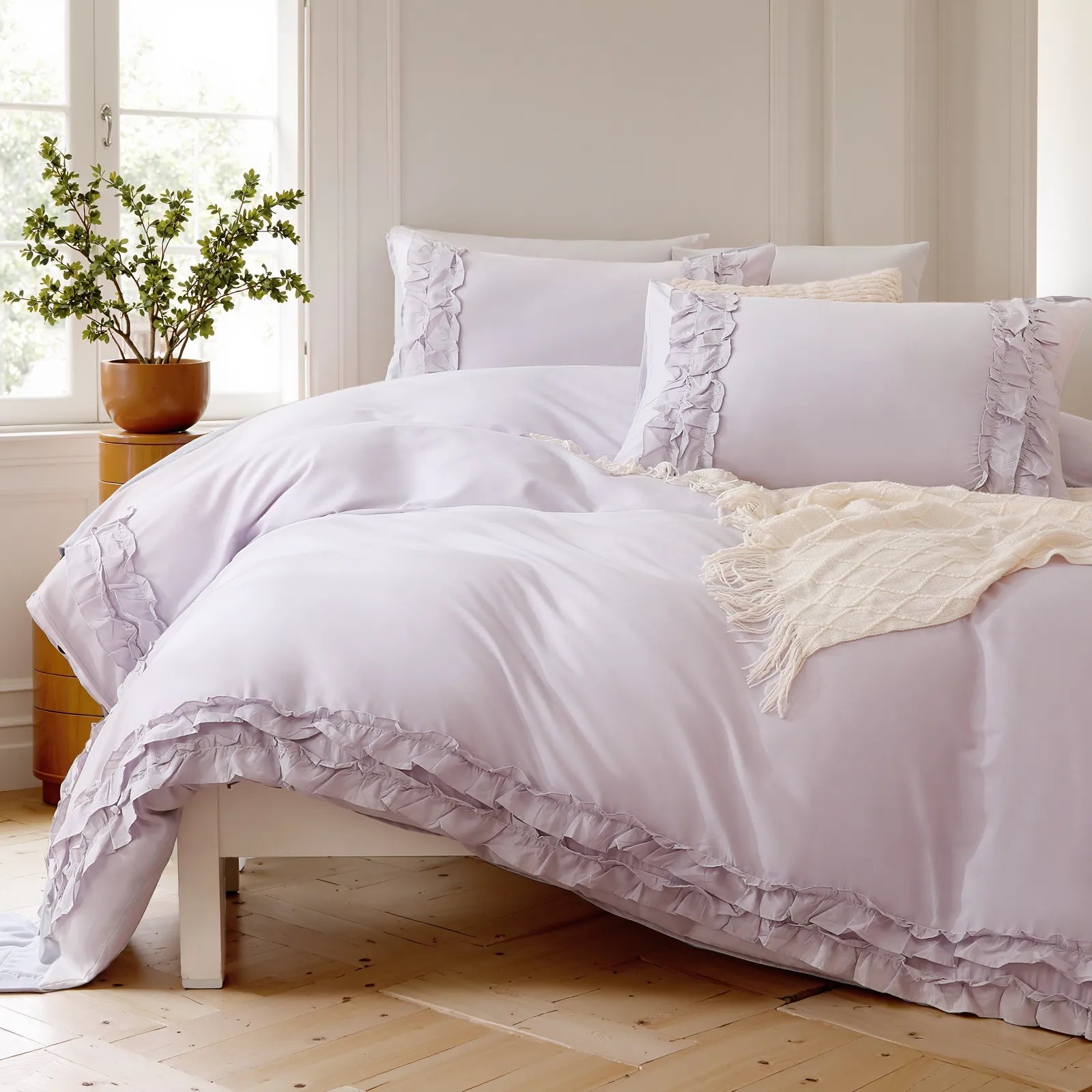 Close-up of lavender cotton ruffle pillows and duvet cover, with a knit throw at the foot of the bed.