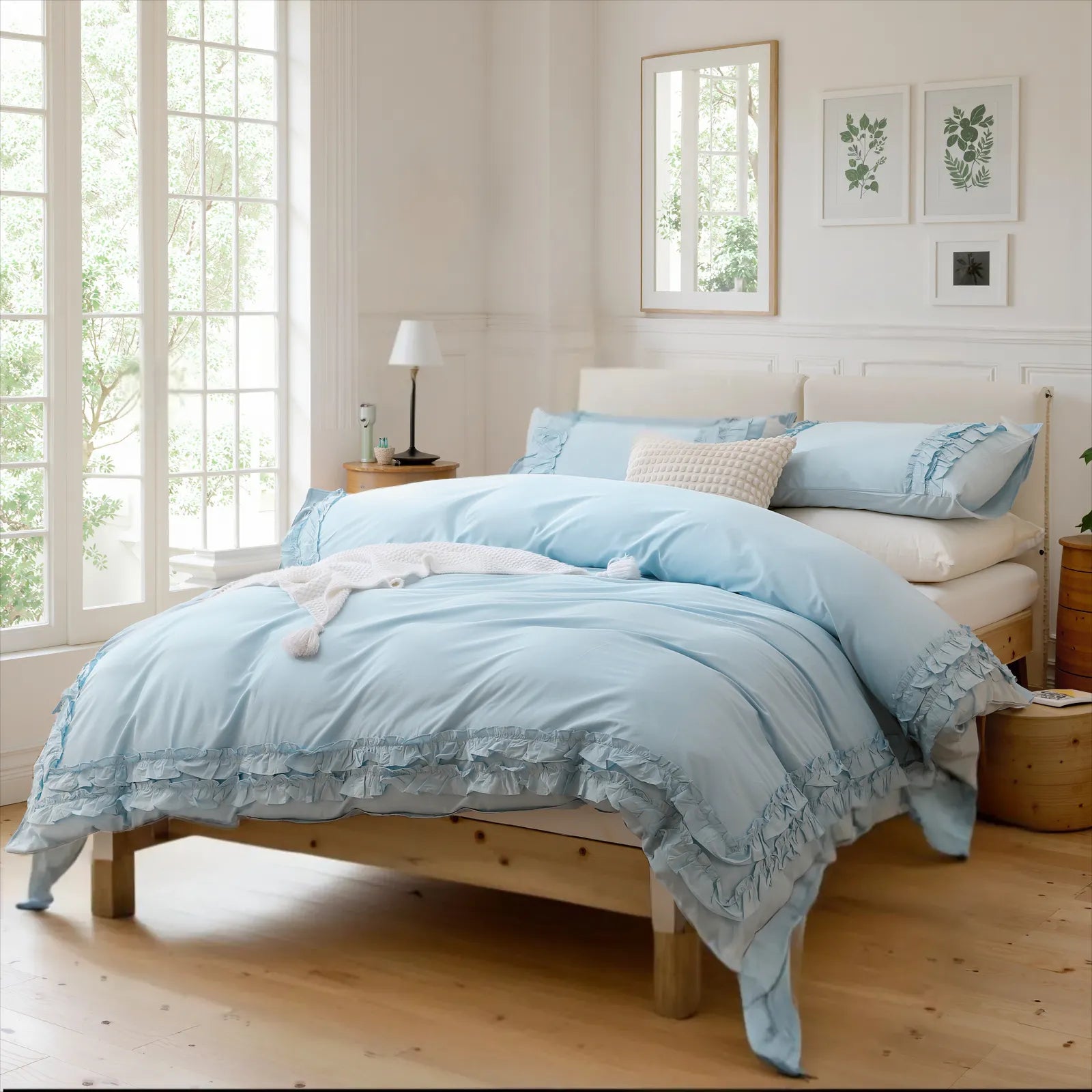 Light blue cotton ruffle bedding set on a bed with a small table and lamp by a large window.