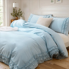 Close-up of a light blue cotton ruffle duvet cover against a white carved headboard with a textured pillow.