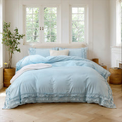 Light blue cotton ruffle duvet cover on a bed with a throw blanket at the foot, near three large windows.