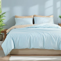 Overview of a light blue duvet on a full bed with symmetric pillows and plants on both sides against a light blue wall.