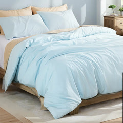 Headboard close-up of a light blue duvet with pillows, books and plants on a wooden nightstand.