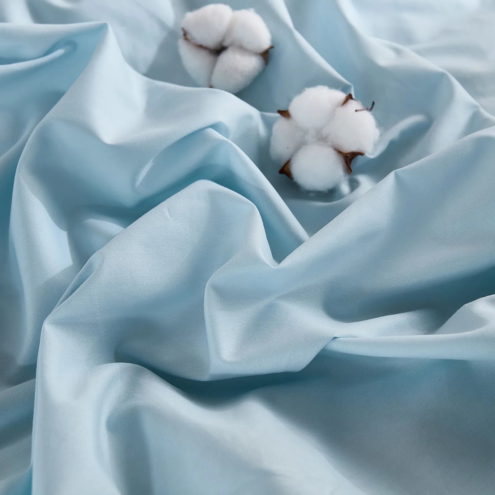 Light blue solid duvet cover with two cotton buds on wrinkled fabric, front view