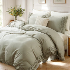 Close-up of light gray cotton double ruffle duvet cover details with a knit pillow and eucalyptus in a glass vase.