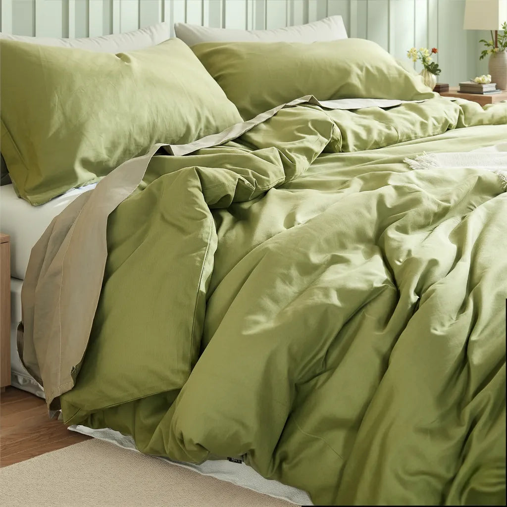 Asymmetric bedroom view with a matcha green duvet set between different-sized wooden tables and a yellow flower vase.