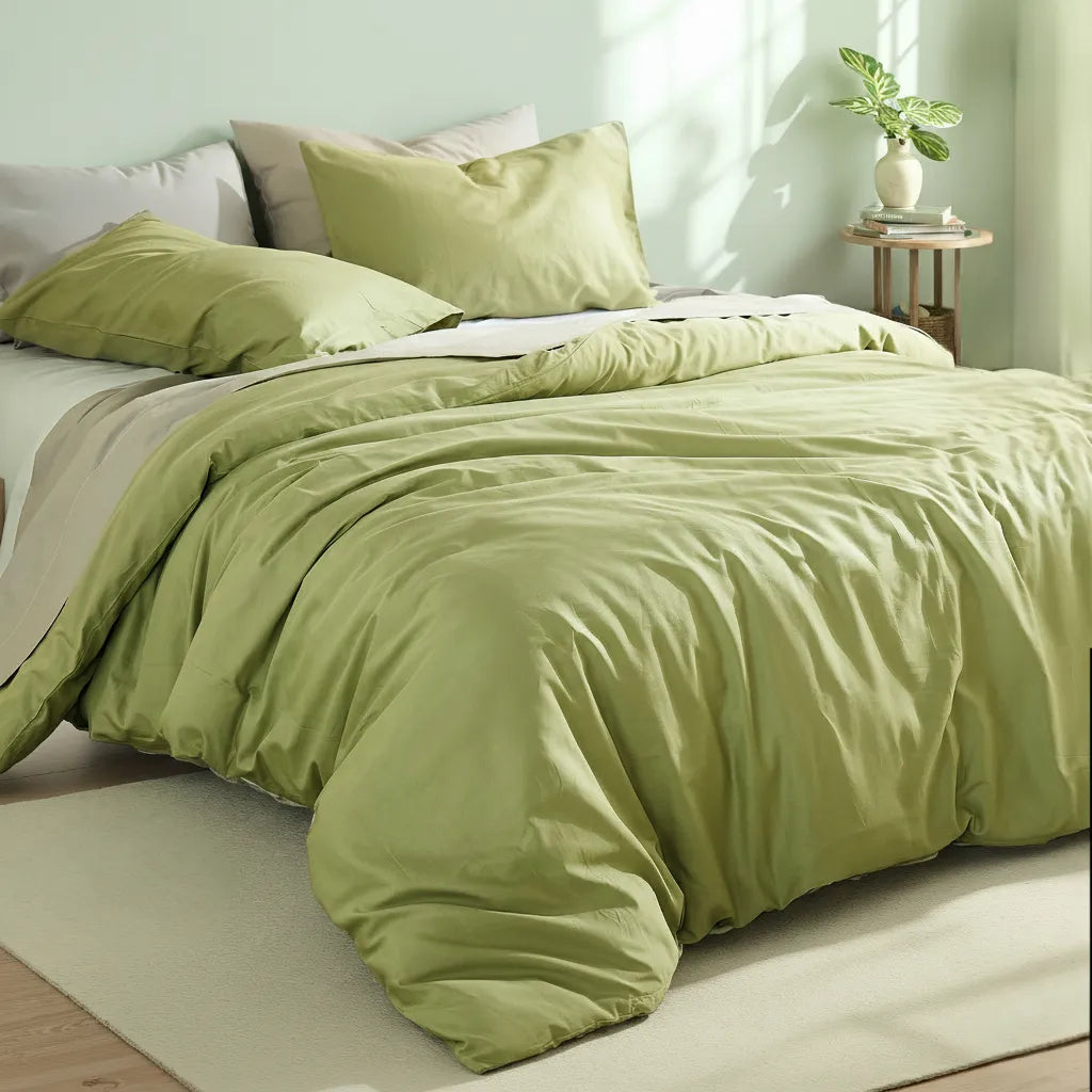 Overhead detail shot of a matcha green duvet with a round wooden side table holding a white vase and green leaves.