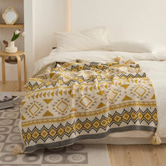 Mustard yellow boho knit throw blanket with tassels spread over a white bed close up view