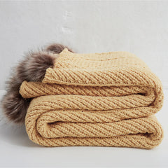 Folded mustard yellow cotton chunky knit throw blanket with brown faux fur pom-poms
