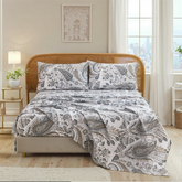 Close up view of cotton neutral paisley sheet set on bed with rustic rattan headboard