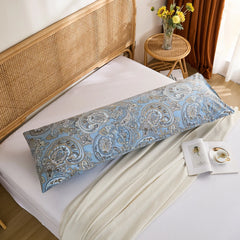 An overhead shot of a long blue paisley print cotton body pillow, laid out on a white bed with an open book and white throw blanket.