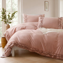 Pink cotton double ruffle duvet cover with a white throw blanket at the foot of the bed, near a vase and wooden buckets.
