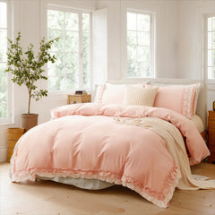 A full bedroom view featuring a pink cotton ruffle bedding set, with a plant and books on a side table.