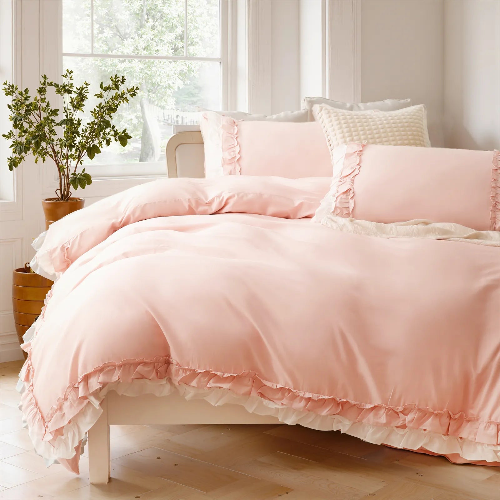 Close-up of a pink cotton double ruffle duvet cover on a white-framed bed with a potted plant.