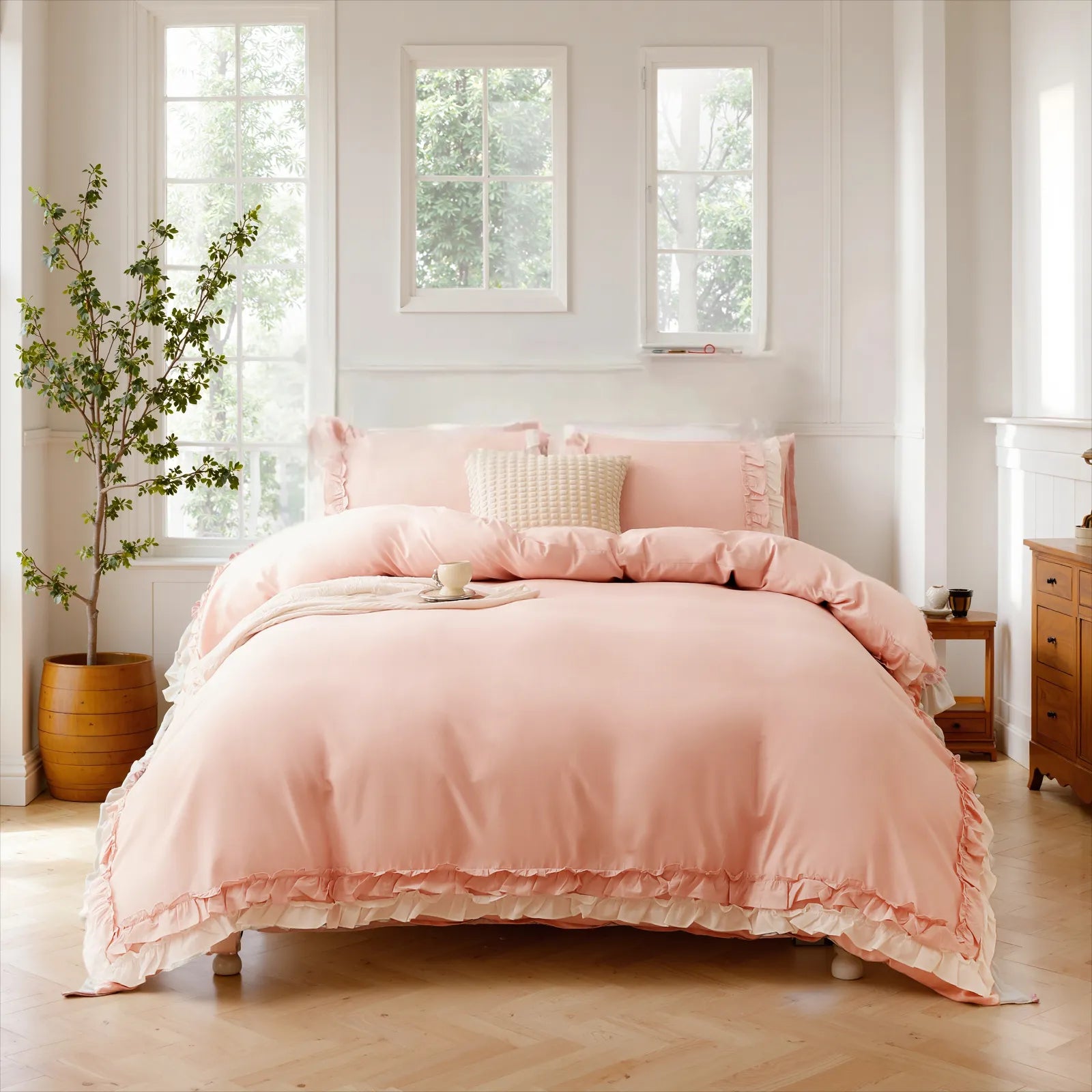 Pink cotton ruffle duvet cover and pillows on a bed with a wooden nightstand and three large windows.