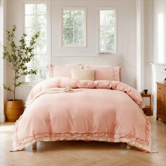 Pink cotton ruffle duvet cover and pillows on a bed with a wooden nightstand and three large windows.