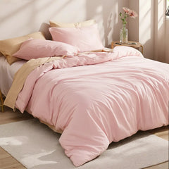 Angled close-up view of the pink duvet with pillows, a round side table with a transparent vase and pink flowers in the foreground.