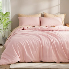 Corner view of a pink solid cotton duvet on a bed with four pillows, a green plant on the left and a wooden nightstand on the right.