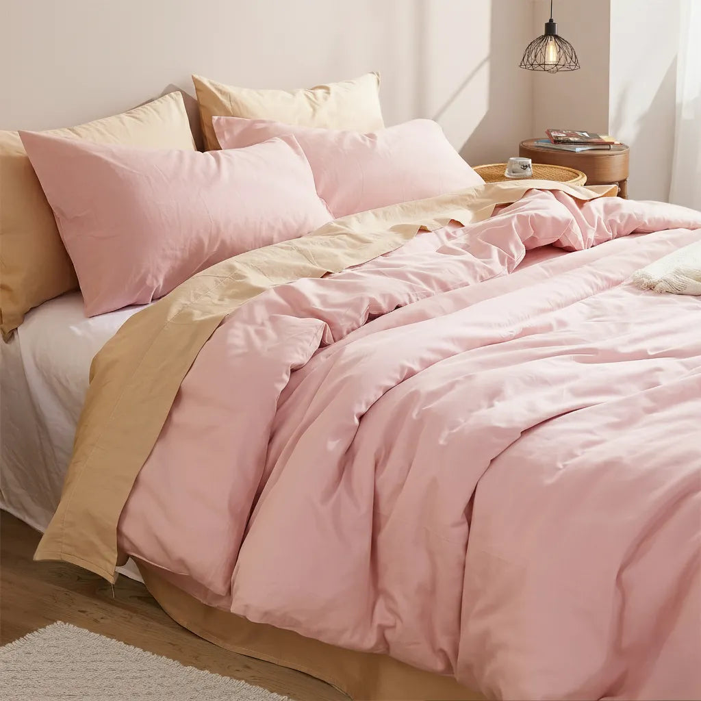 Side-front angle of the pink duvet set showing the bedskirt contrast, with a wooden table and black pendant lamp in the composition.