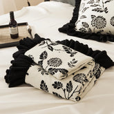 A neatly folded ruffled microfiber blanket, showing its soft texture and beautiful black leaf print.