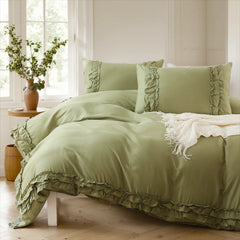 Sage green cotton double ruffle duvet cover on a bed with a white knit throw and round side table with plants.