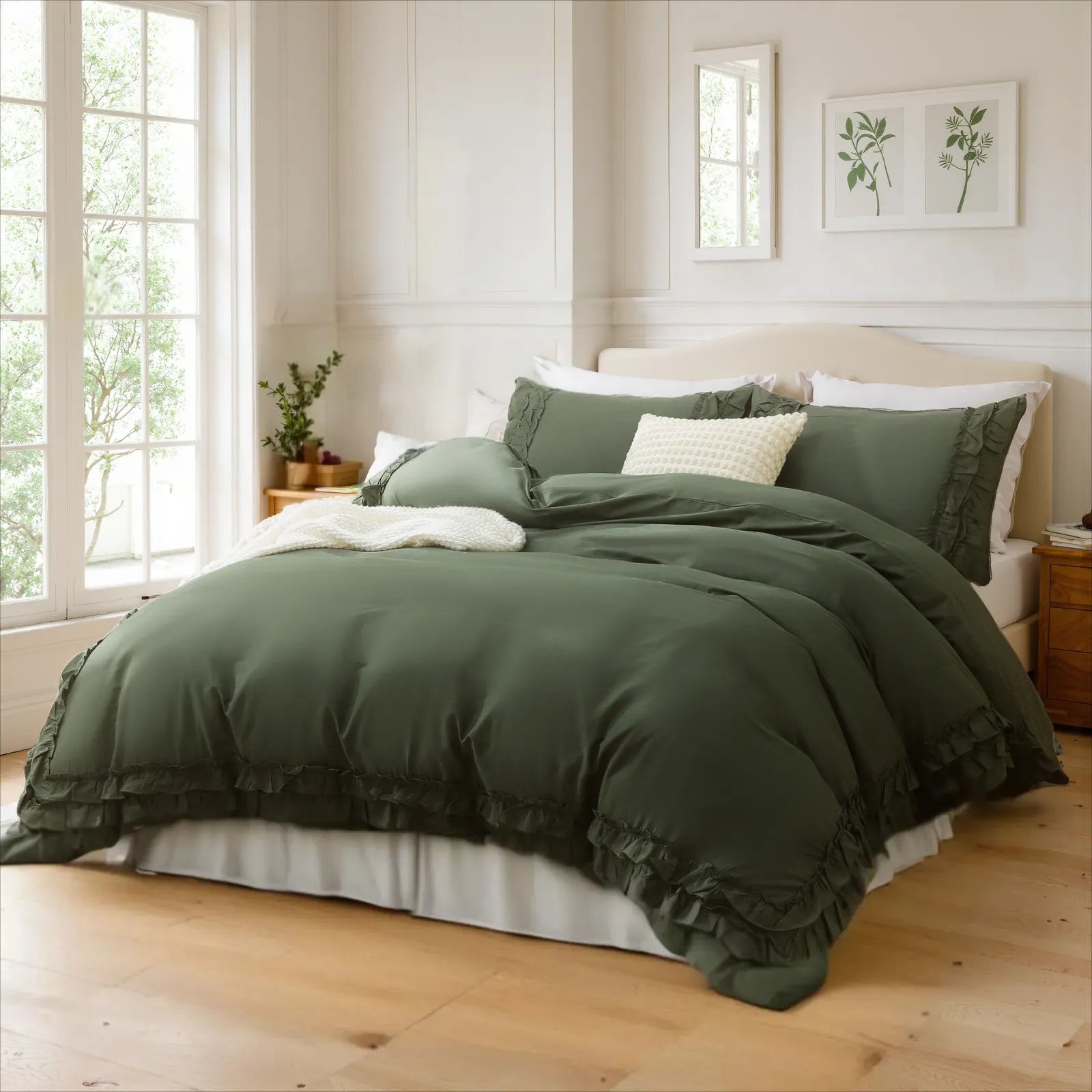 A bed dressed with a sage green cotton duvet, an assortment of pillows, and botanical prints on the wall.