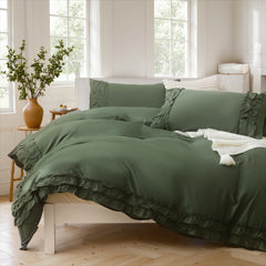 Side view of a sage green cotton ruffle duvet cover set with a white throw blanket and a wooden side table.