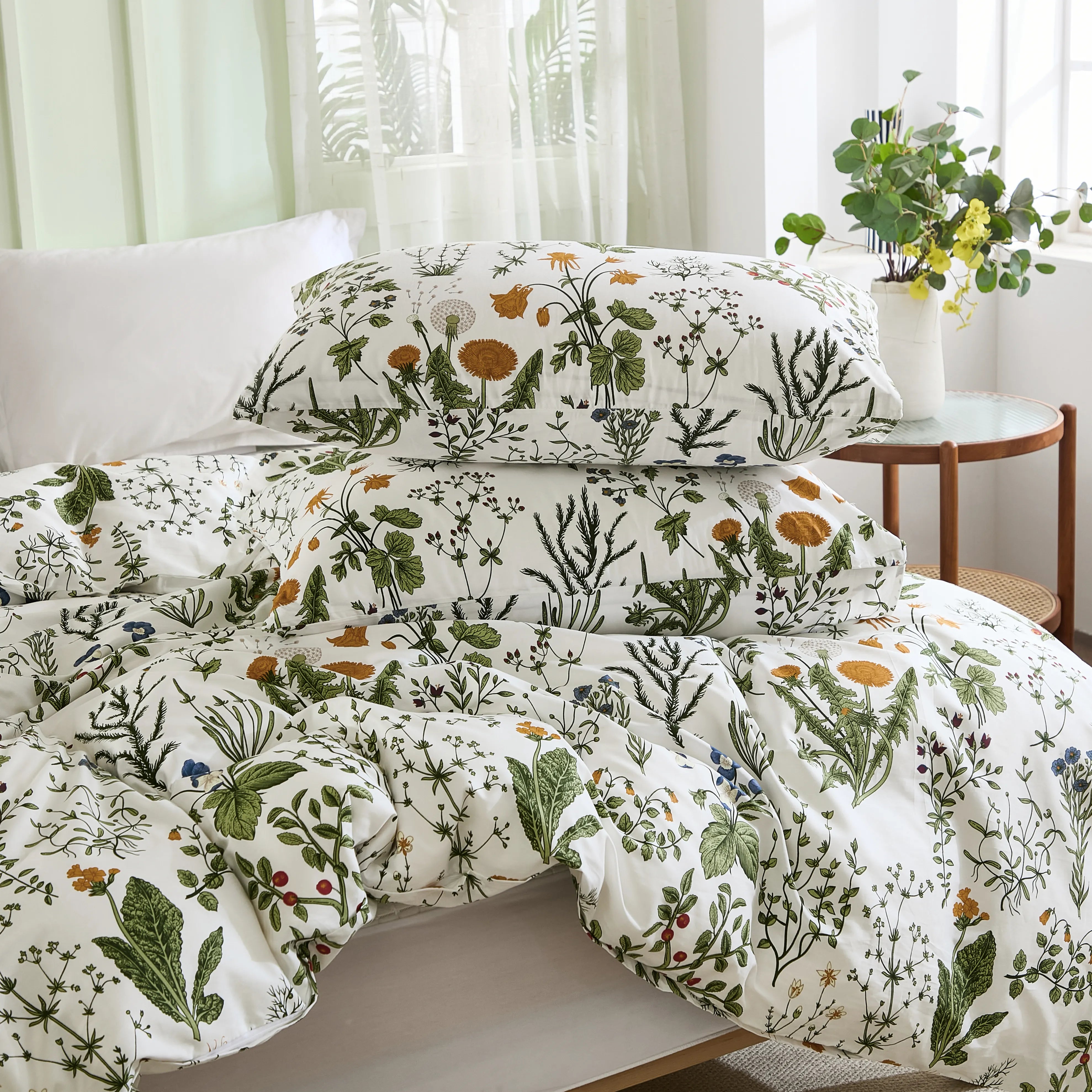 A stack of two pillows and a folded comforter from a sage green floral duvet set on a white bed.
