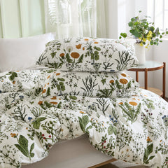 A stack of two pillows and a folded comforter from a sage green floral duvet set on a white bed.