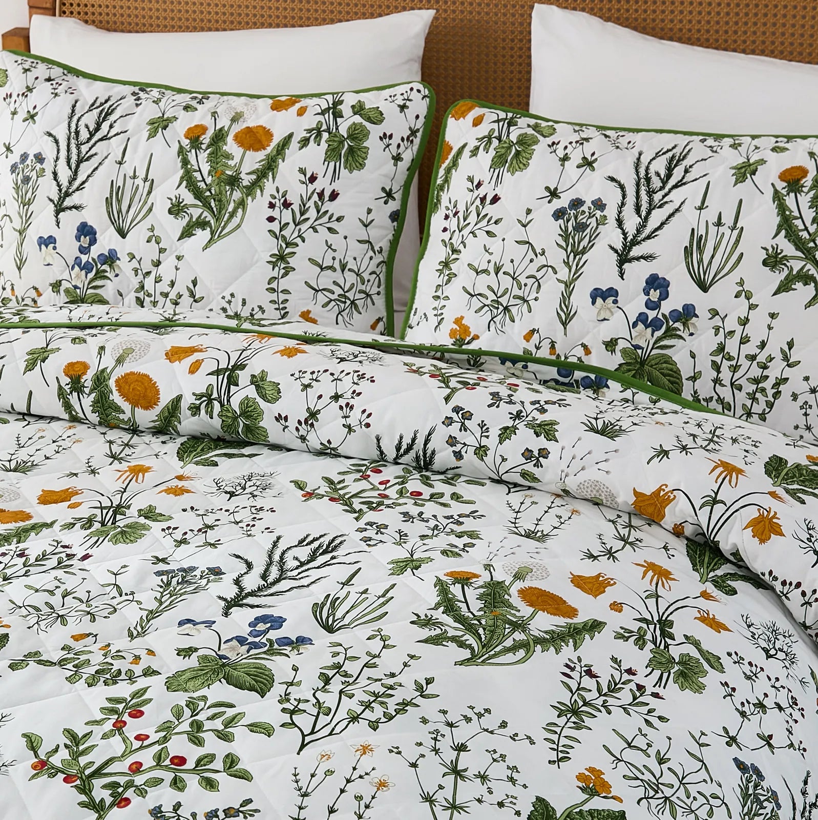 A detailed view of the sage green floral quilt set from a bed corner.