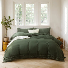 Sage green cotton ruffle bedding on a bed against three large windows with a peaceful tree view and a woven basket.
