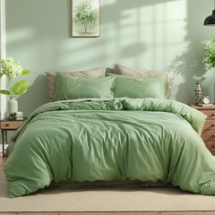 Sage green solid cotton duvet with four pillows, paired with an art print and glass vase with greenery on a dark wood nightstand.