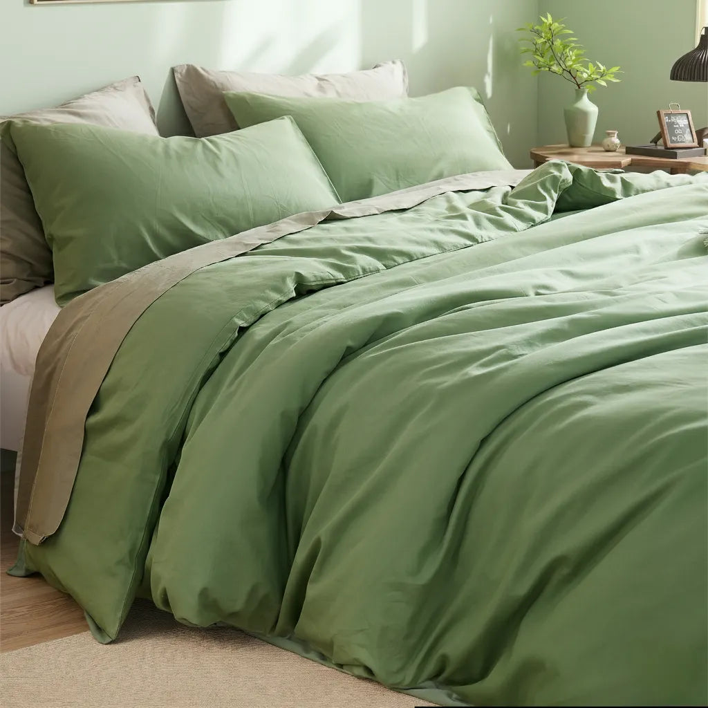 Sage green cotton duvet on bed with tonal pillows over a light rug, plant in terracotta pot catching sunlight.