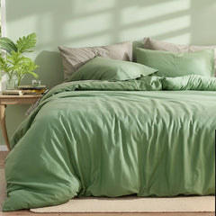 Soft sage green cotton duvet set with pillows, accompanied by a potted plant and woven lamp on a wooden side table.