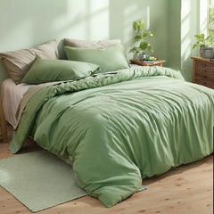 Sage green duvet on bed between matching wooden nightstands, one with white flowers in a vase under a tree silhouette painting.