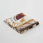 A studio shot of a perfectly folded sand yellow bohemian tassel blanket, highlighting its material and beautiful color.