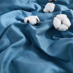 Top view of soft blue duvet with three cotton blooms on fabric surface