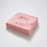 Neatly folded soft pink cotton knit throw blanket with cream fringe trim and bobble texture