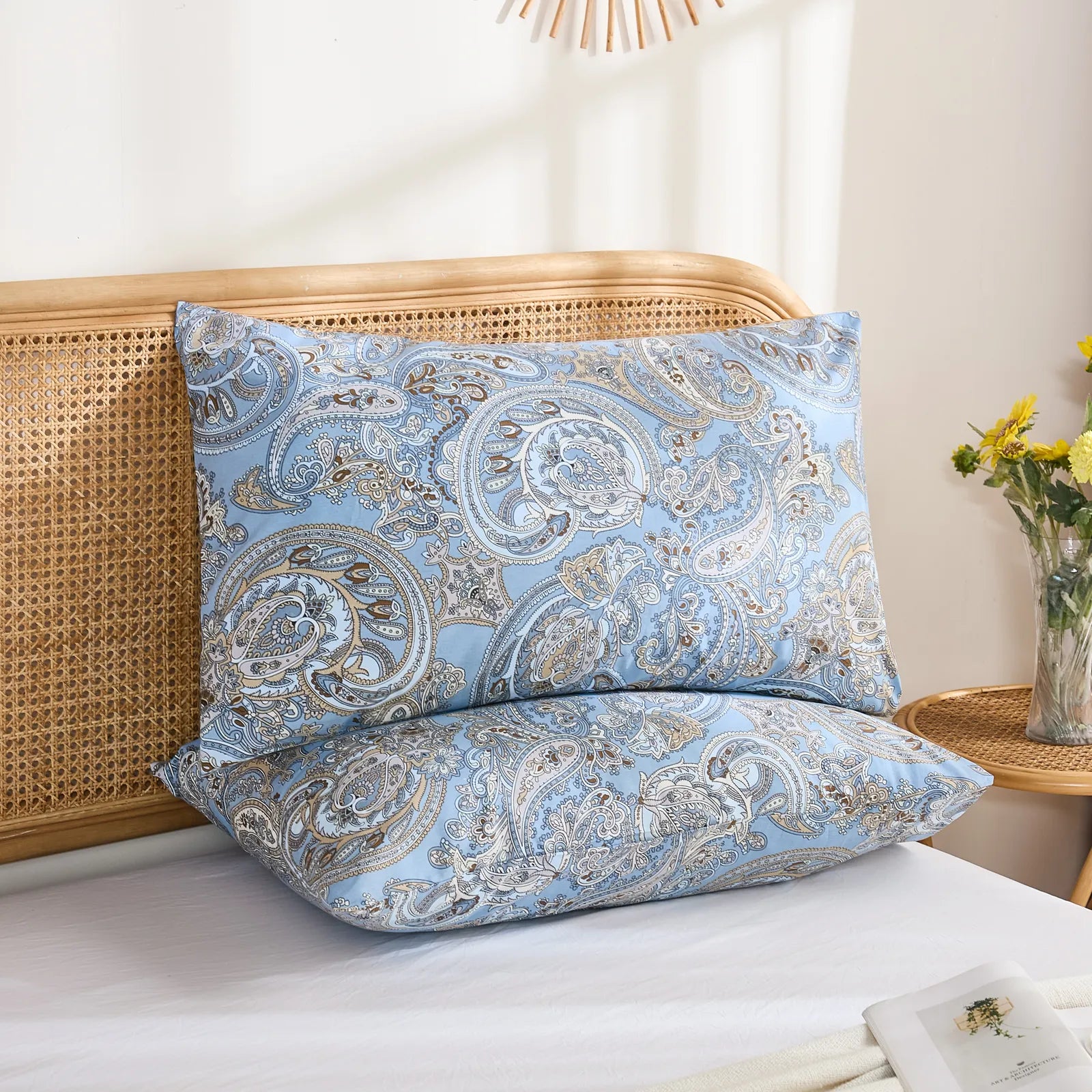 A close-up shot of two light blue cotton paisley print pillowcases stacked on a bed, highlighting the intricate pattern.