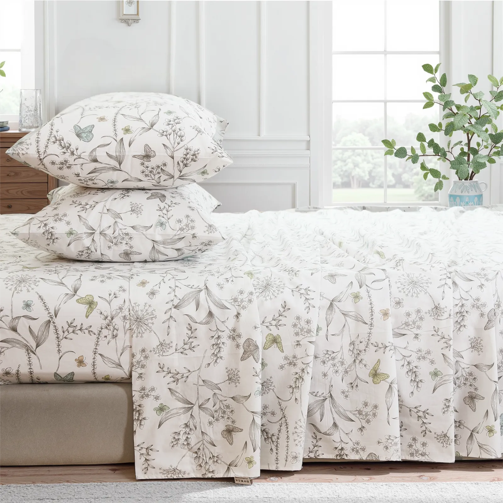 Stacked cotton botanical print pillows on sheet set with full drape on the side of the bed