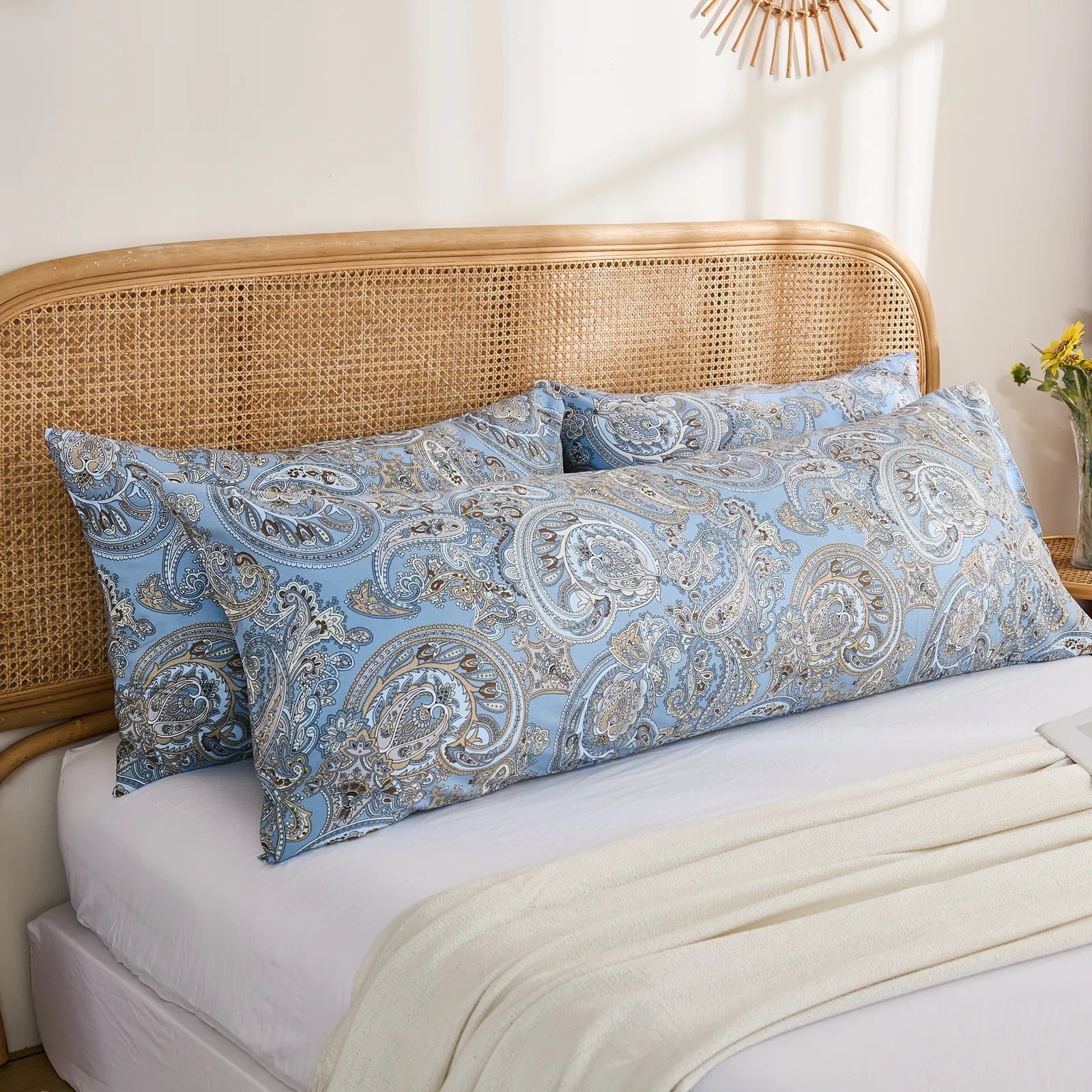 A pair of long blue paisley print cotton body pillows placed together on a bed, with a white blanket draped across the front.