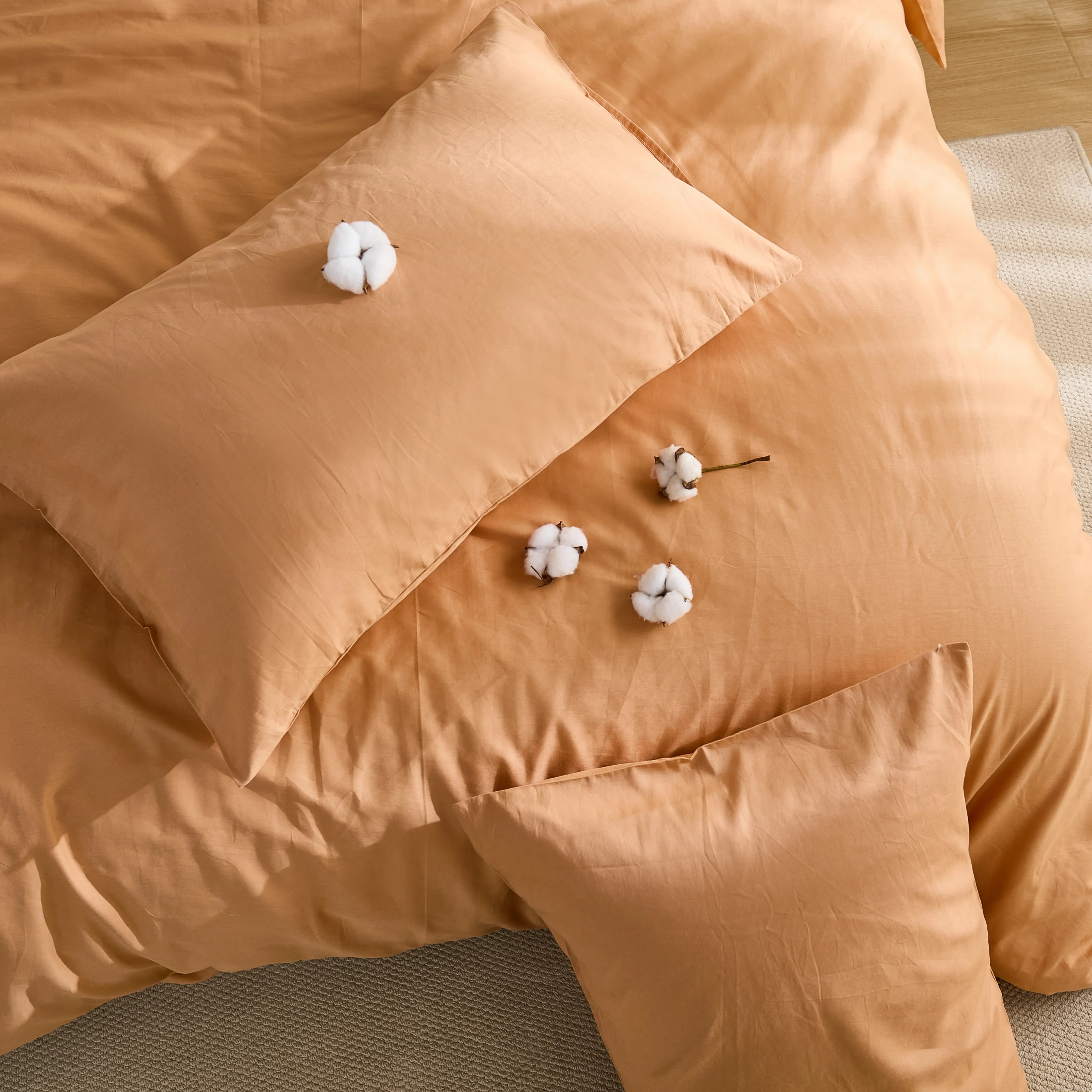 Warm orange duvet with scattered cotton balls and two pillows on surface