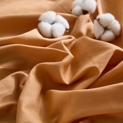 Close-up of warm orange fabric with three white cotton blooms contrast