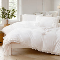 Close-up view of a soft white cotton ruffle duvet cover and a stack of pillows on the bed.