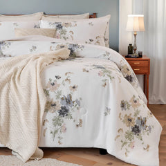 Angled view of a bed with a white floral comforter set, beige knit blanket, and a wood nightstand